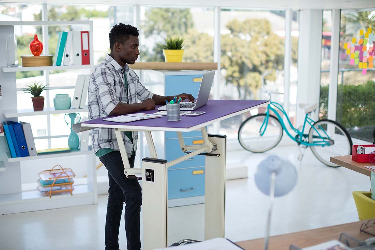 A man using a laptop on an adjustable standing desk.