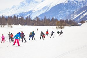  group of people cross-country skiing on a snowy trail surrounded by trees and mountains. 