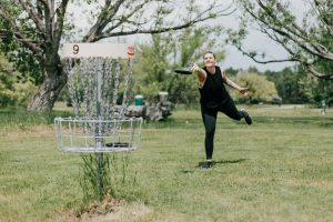 A woman throwing a disc at a disc golf course basket target.
