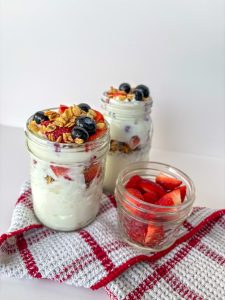 Berry and granola yogurt parfaits in jars on a table.