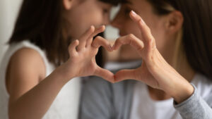 A mother and daughter making a heart shape with their hands.