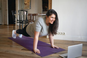 A smiling woman doing push-ups in front of a laptop.