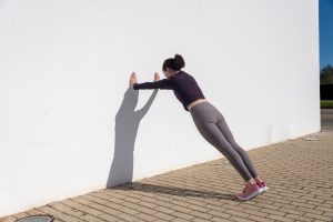 A woman doing a wall push-up. A woman doing a wall push-up.