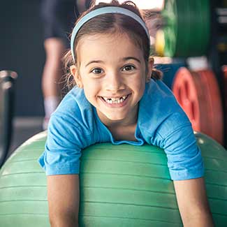 little girl smiling while hanging over a yoga ball