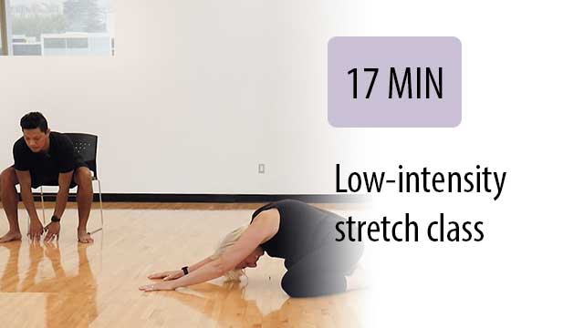 instructor leading seated student with stretch in gym