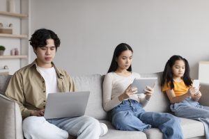 A group of teenagers using electronic devices on a couch. They are engaging in too much screen time.