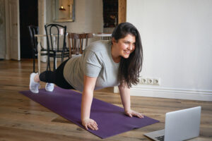 Une femme souriante fait du yoga devant un ordinateur portable.