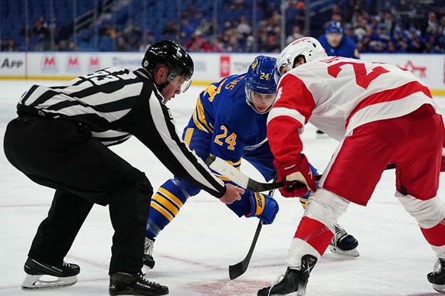 Un arbitre laisse tomber une rondelle de hockey sur la glace pour Dylan Cozens et un joueur de hockey de l’équipe adverse.