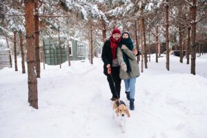 Un homme et une femme promenant un chien sur un sentier naturel enneigé.