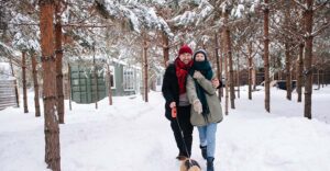 A man and woman walking a dog on a snow-covered nature trail.