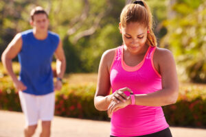 A man jogging beside a woman in exercise clothes checking her smart watch.