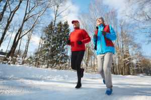 Two people jogging on a snow-covered nature trail surrounded by trees.