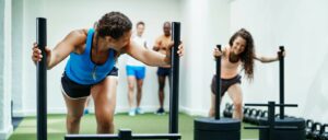 Two women working out with machines in a gym. Exercising with others is helpful in achieving goals.