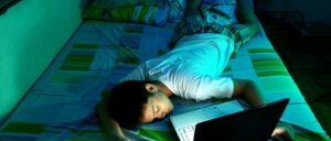 A teenage boy sleeping on a bed in front of a laptop. He's had too much screen time.