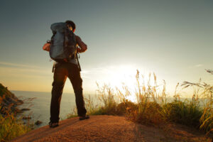 A person standing on a cliff overlooking a body of water for some fresh air.