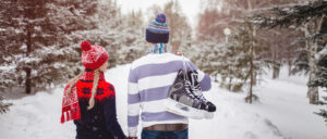 A couple walking on a snow-covered nature trail while carrying skates.