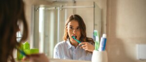 A woman brushing her teeth in the mirror. She has managed to form a habit.
