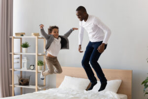 A father and son jumping on a bed. 