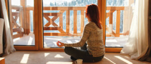 A woman practicing mindfulness by meditating while looking out the window.