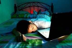 A teenage boy sleeping on a bed in front of a laptop. Teen screen use is at an all-time high. 