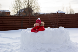 A kid sitting in a snow fort. 