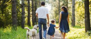 couple with their kid and their dog walking in a forest