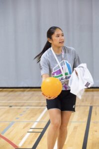 Olivia Ho holding a yellow basketball in a gymnasium. 