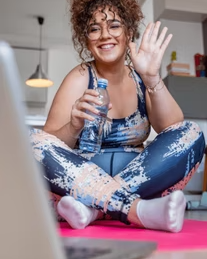 Une femme assise sur un tapis de yoga avec une bouteille d’eau regarde un écran d’ordinateur