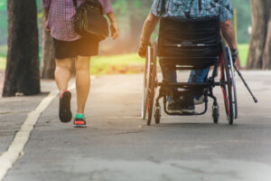 Une personne marchant à côté d’une personne en fauteuil roulant sur un trottoir. 