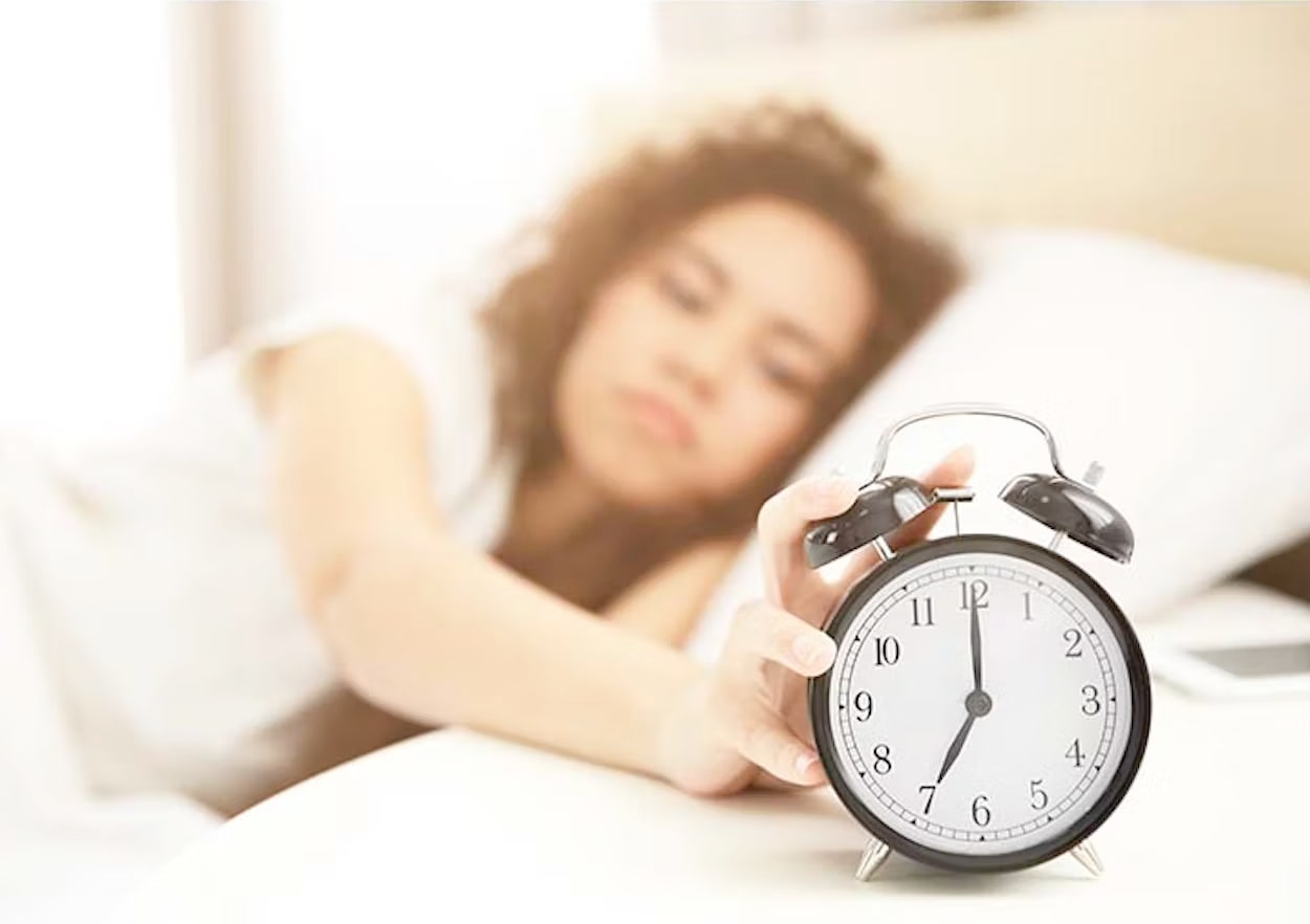Girl in bed turning off the alarm clock