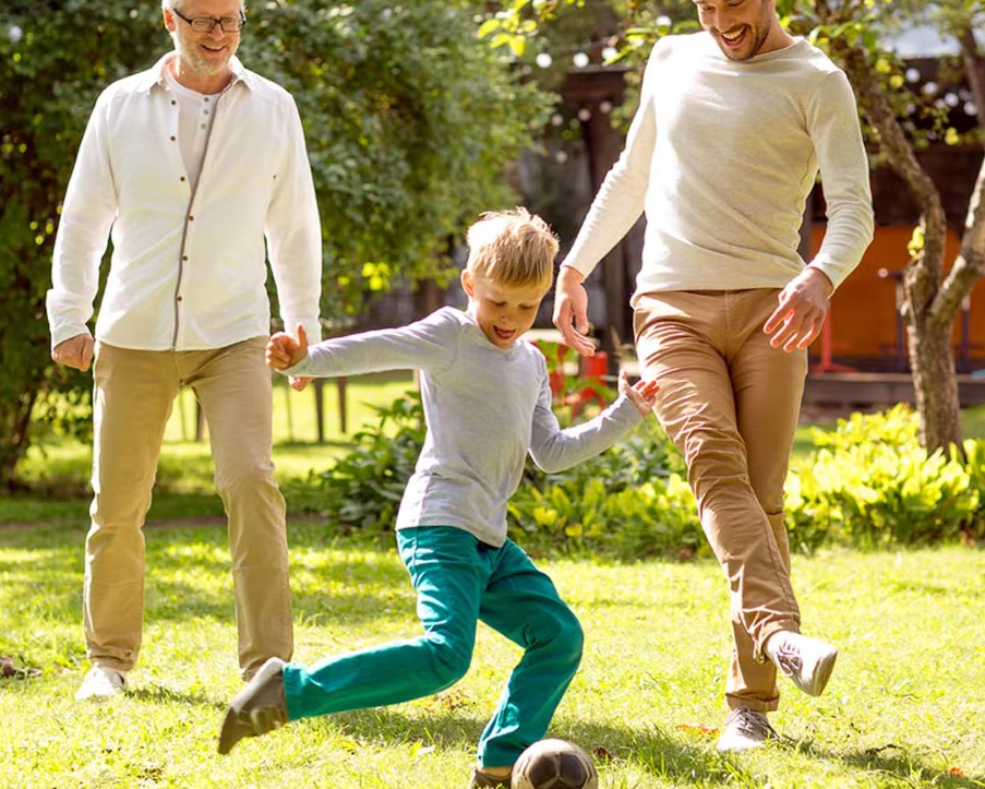 Elderly man, young man and a kid playing soccer in the yard