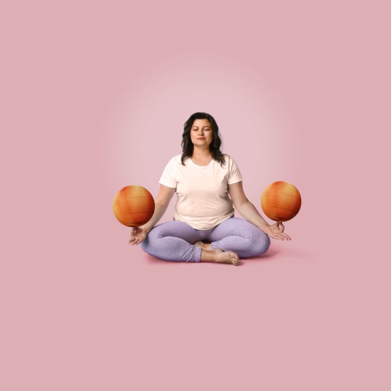 A woman sitting cross legged balancing two basketballs