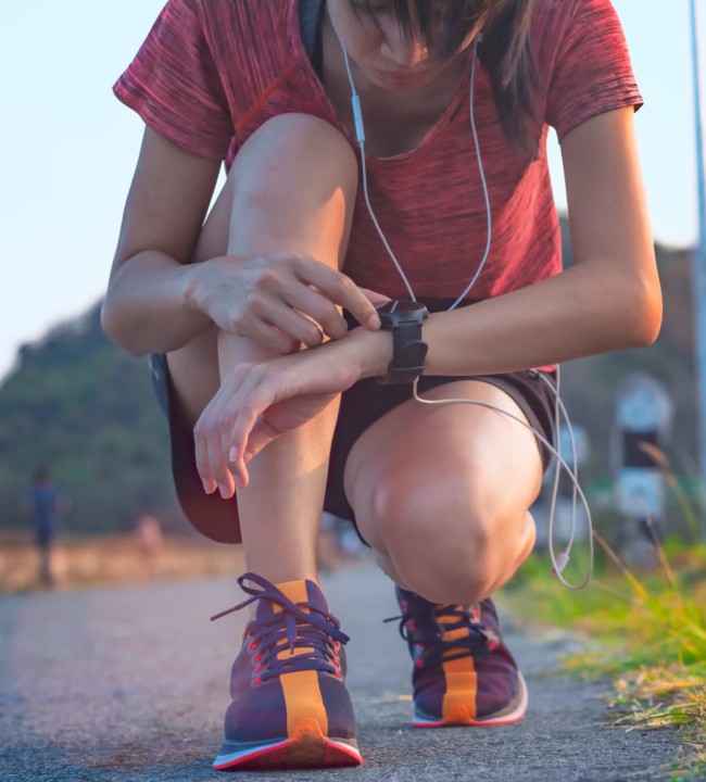 A woman kneeling and checking her smart watch after running