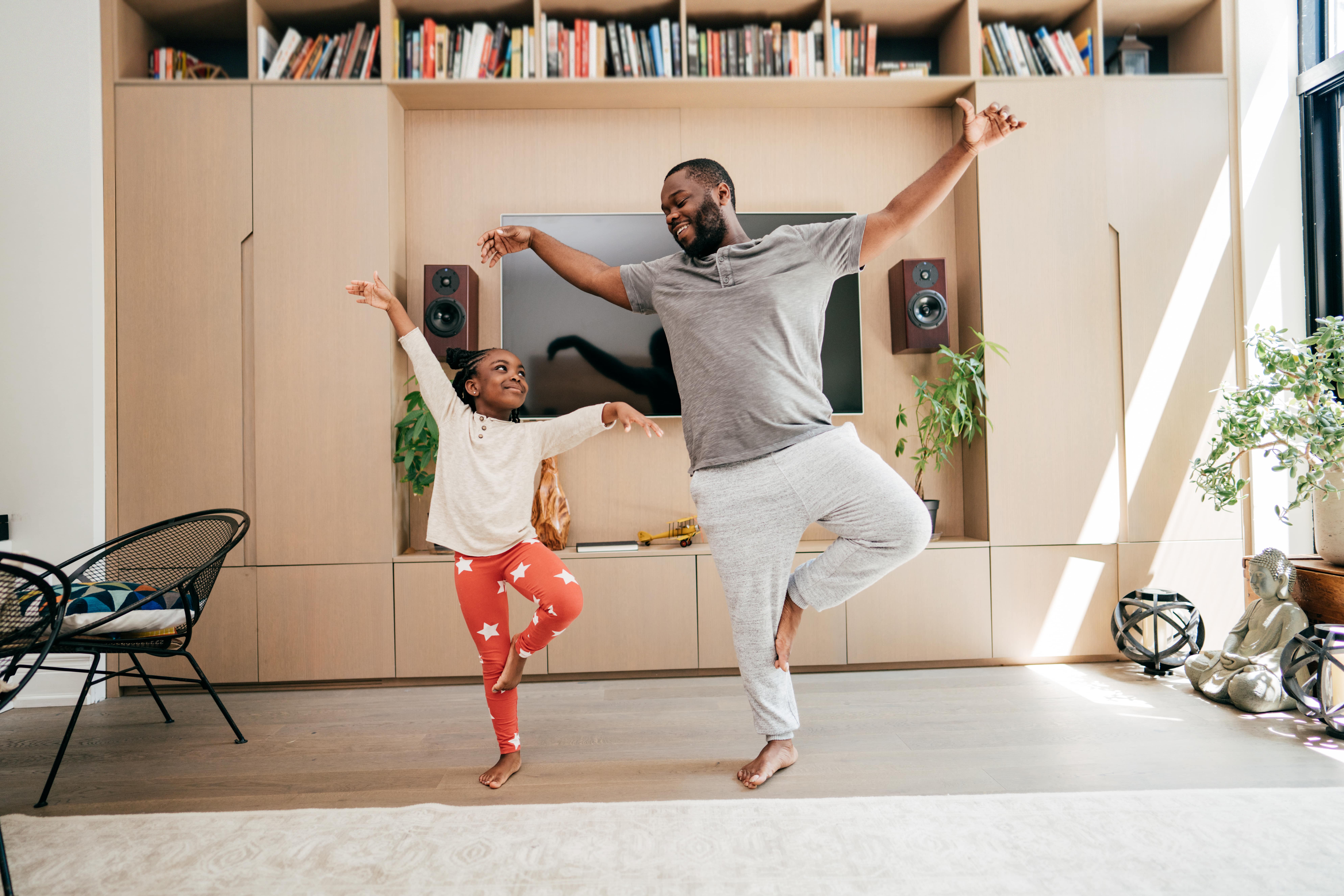 A little girl and an adult doing a yoga stance in the living room