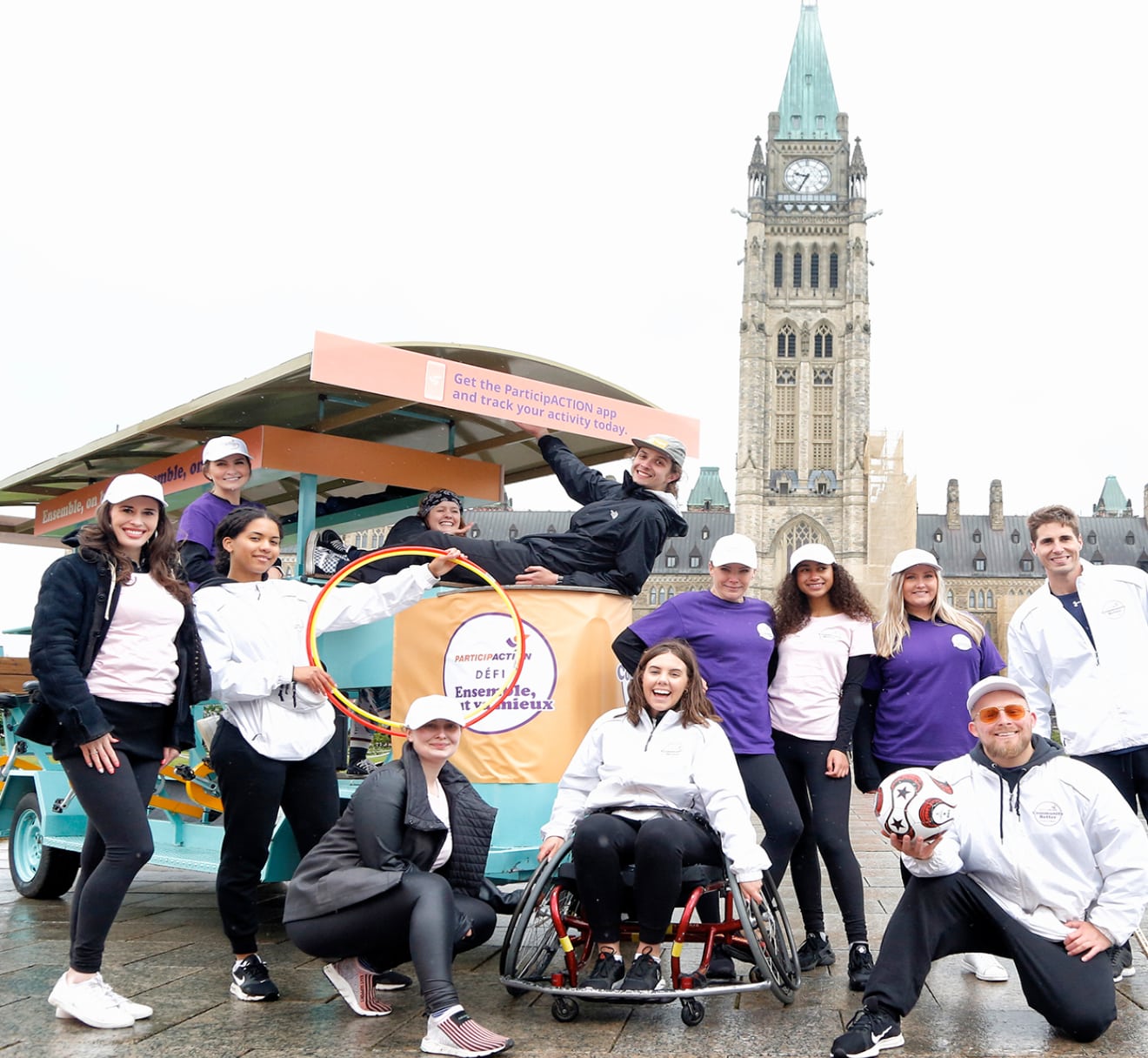 A group of 12 adults smiling and posing in front of Parliament Hill during the Community Better Challenge