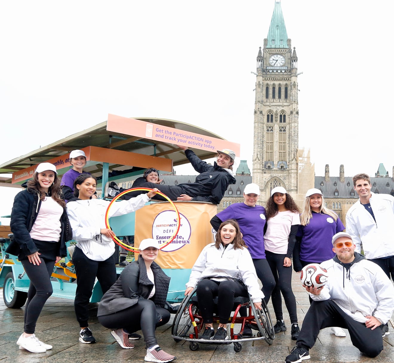 Un groupe de 12 adultes souriants pose pour une photo devant la Colline du Parlement dans le cadre du défi Ensemble, tout va mieux