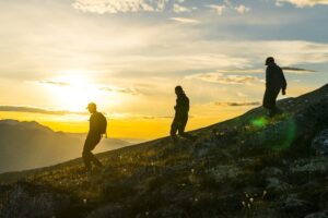 Three people walking down a hill at sunset