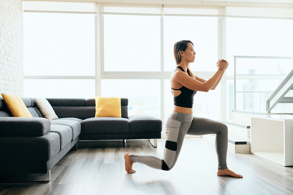 Woman in yoga suit doing lunges in a living room