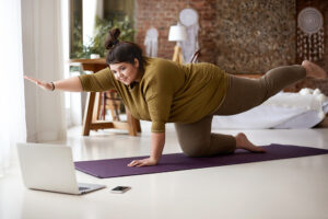 Woman stretching on top of a yoga mat looking at a laptop