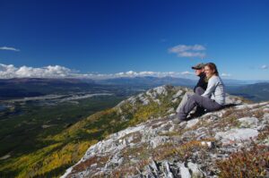 2 people sitting on a cliff overlooking mountains