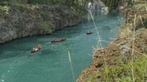 Three red canoes traveling down a river in the Yukon