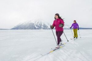 Deux personnes faisant du ski de fond avec une montagne enneigée en arrière-plan.