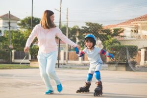 A mom holding hands with her child who is rollerblading on a driveway.  