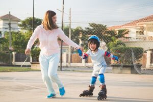 Une maman tient la main de son enfant qui fait du patin à roulettes dans une allée. 