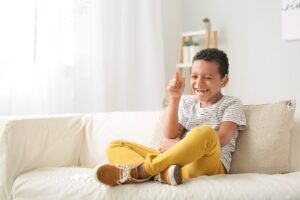 A smiling boy sitting on a couch in a living room. 