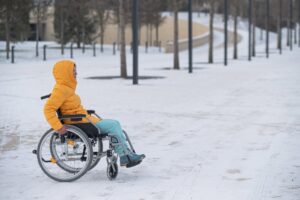 Une personne en fauteuil roulant avance sur passage piéton enneigé. 