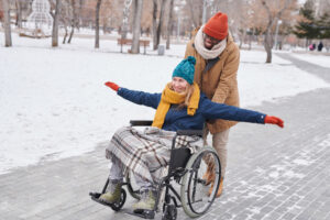 A smiling man pushing a smiling woman in a wheelchair at a park during winter. 