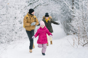 A man, woman and child running on a snow-covered nature trail surrounded by trees. 