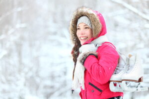 A smiling woman in a winter coat carrying a pair of ice skates.