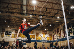 A girl playing the Inuit game called one-foot high kick in a gymnasium. 